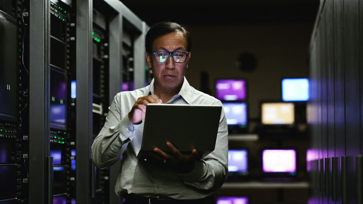 An IT manager reads a security alert on a laptop in a server room at night