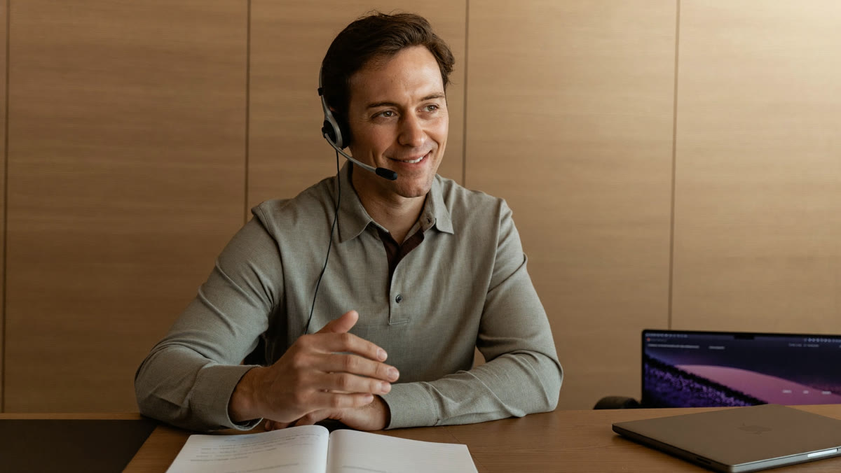 A sales rep with a headset smiles during a call at his desk